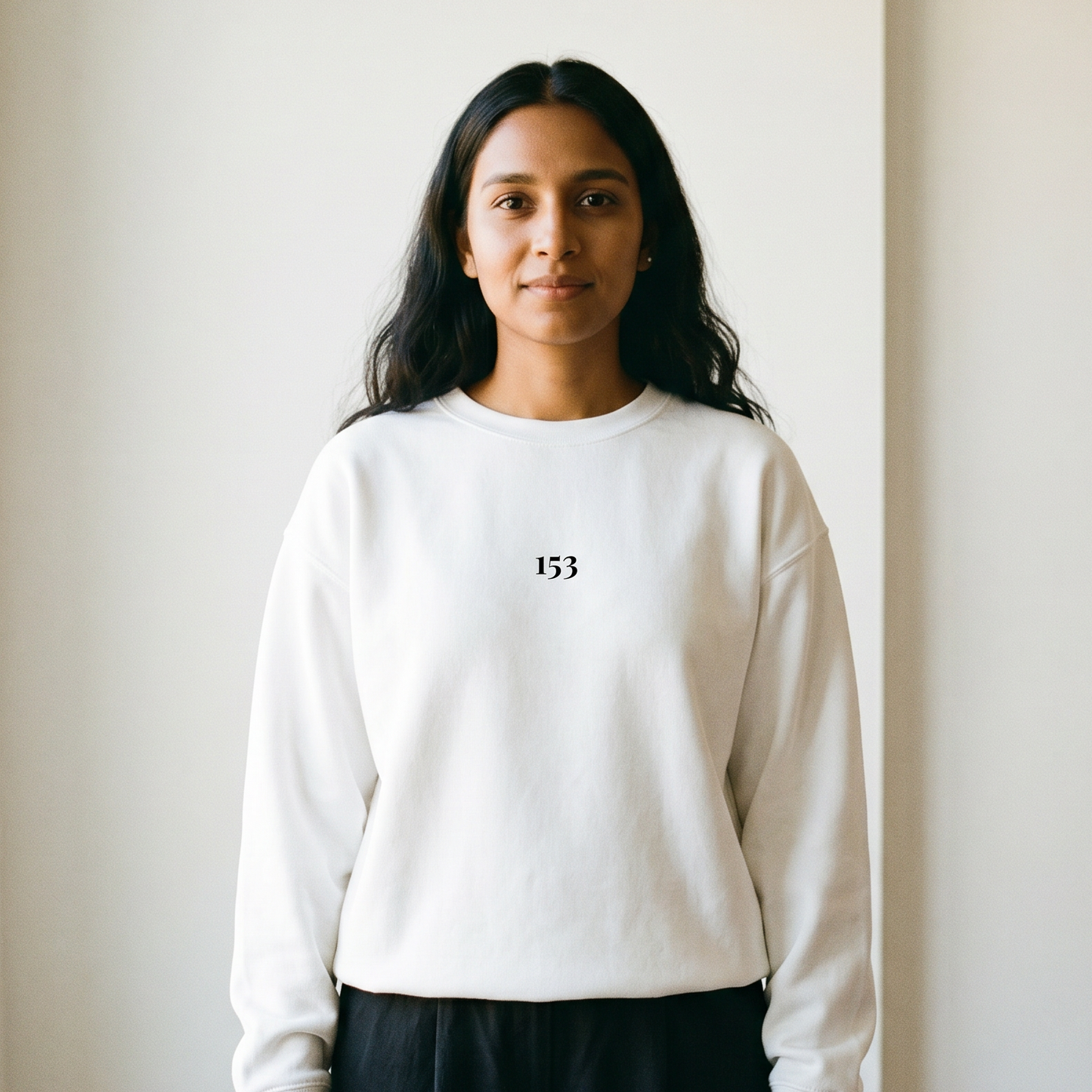 Person wearing a white sweatshirt with a 153 logo, standing against a plain wall.