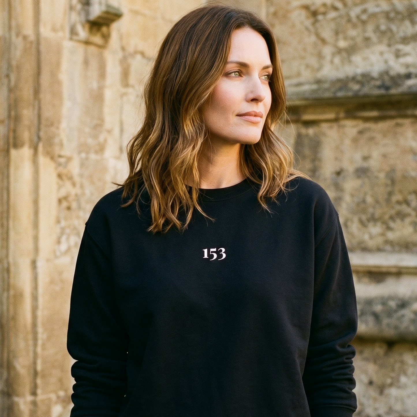 Woman wearing a black sweatshirt with the number 153 in front of a stone building.