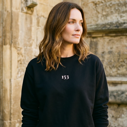 Woman wearing a black sweatshirt with the number 153 in front of a stone building.