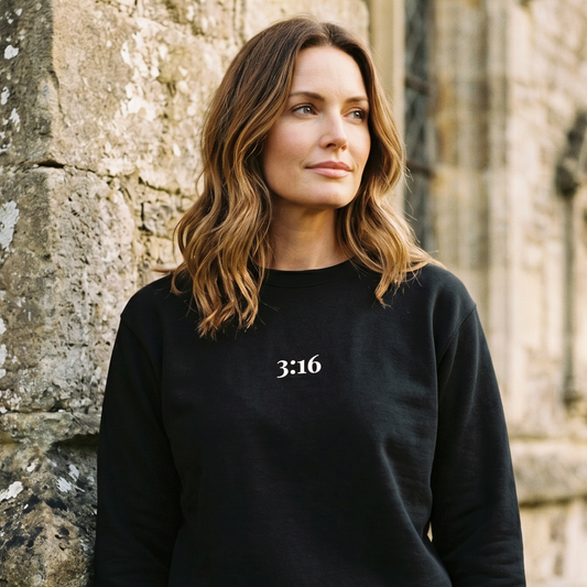 Woman wearing a black sweatshirt with '3:16' on it, standing against a stone wall.