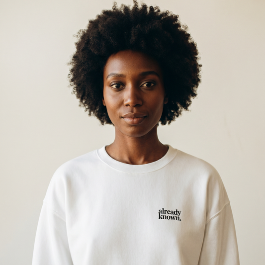 Person wearing a white sweatshirt with 'already known' text on a plain background