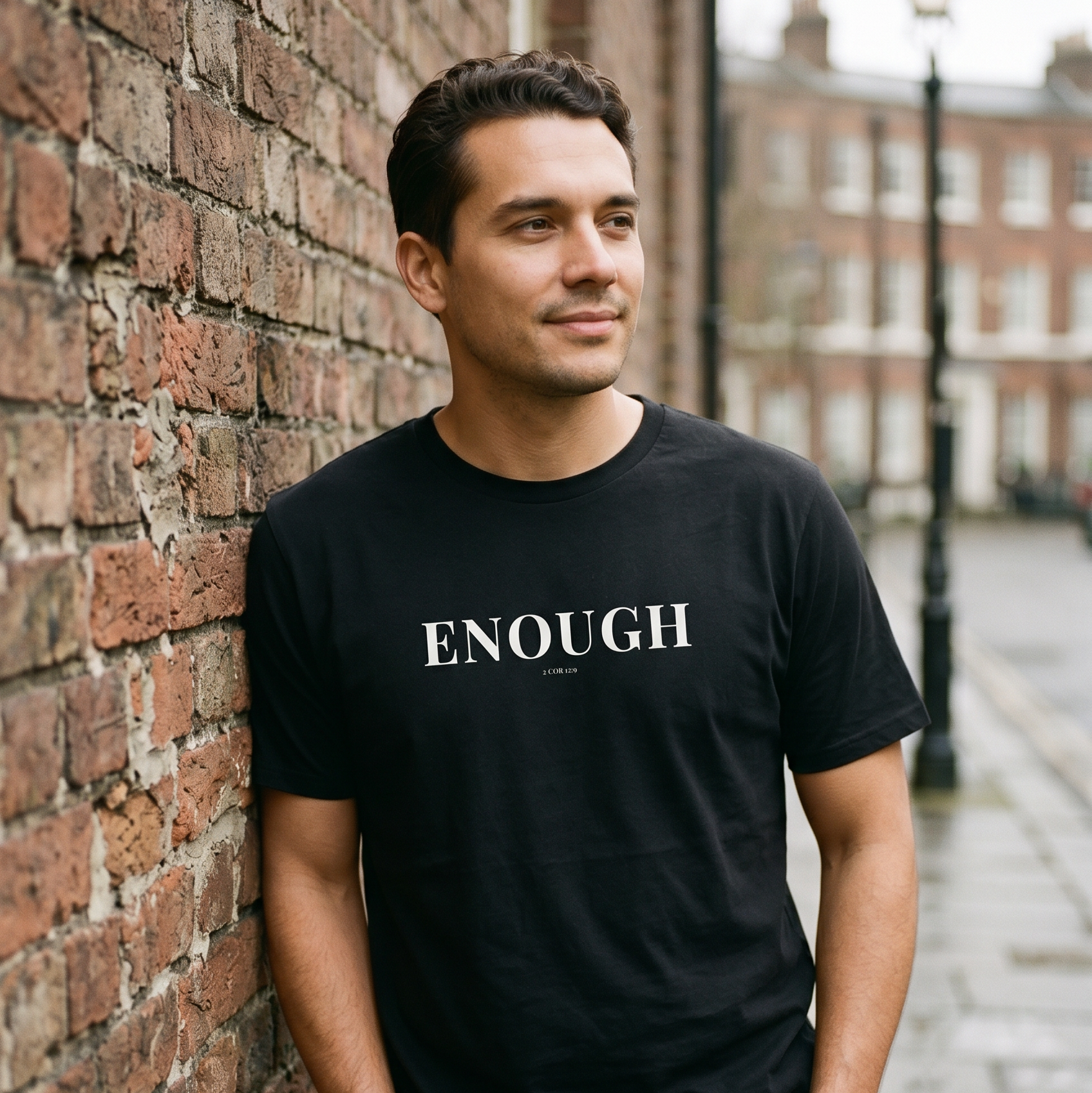 Man wearing a black t-shirt with 'ENOUGH' text, standing against a brick wall.