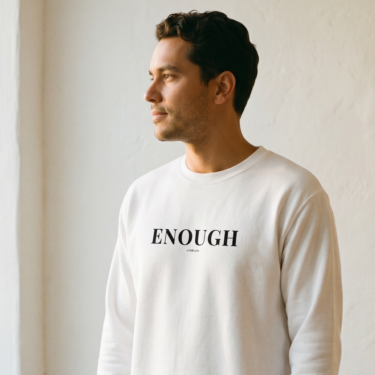 Man wearing a white sweatshirt with 'ENOUGH' text in a minimal indoor setting