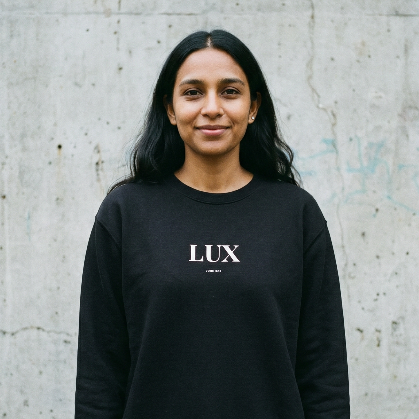Person wearing a black sweatshirt with 'LUX' logo against a concrete wall.
