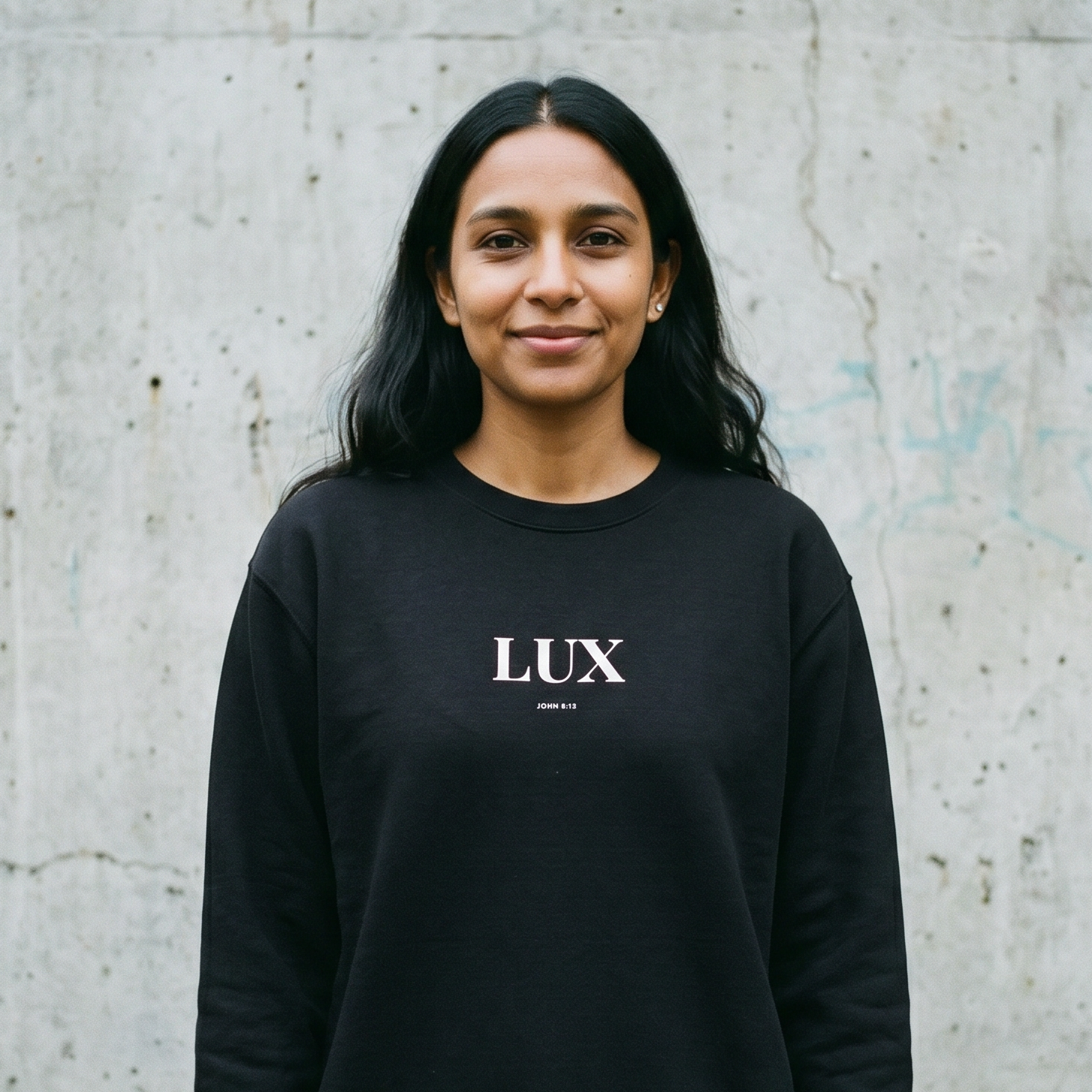 Person wearing a black sweatshirt with 'LUX' logo against a concrete wall.