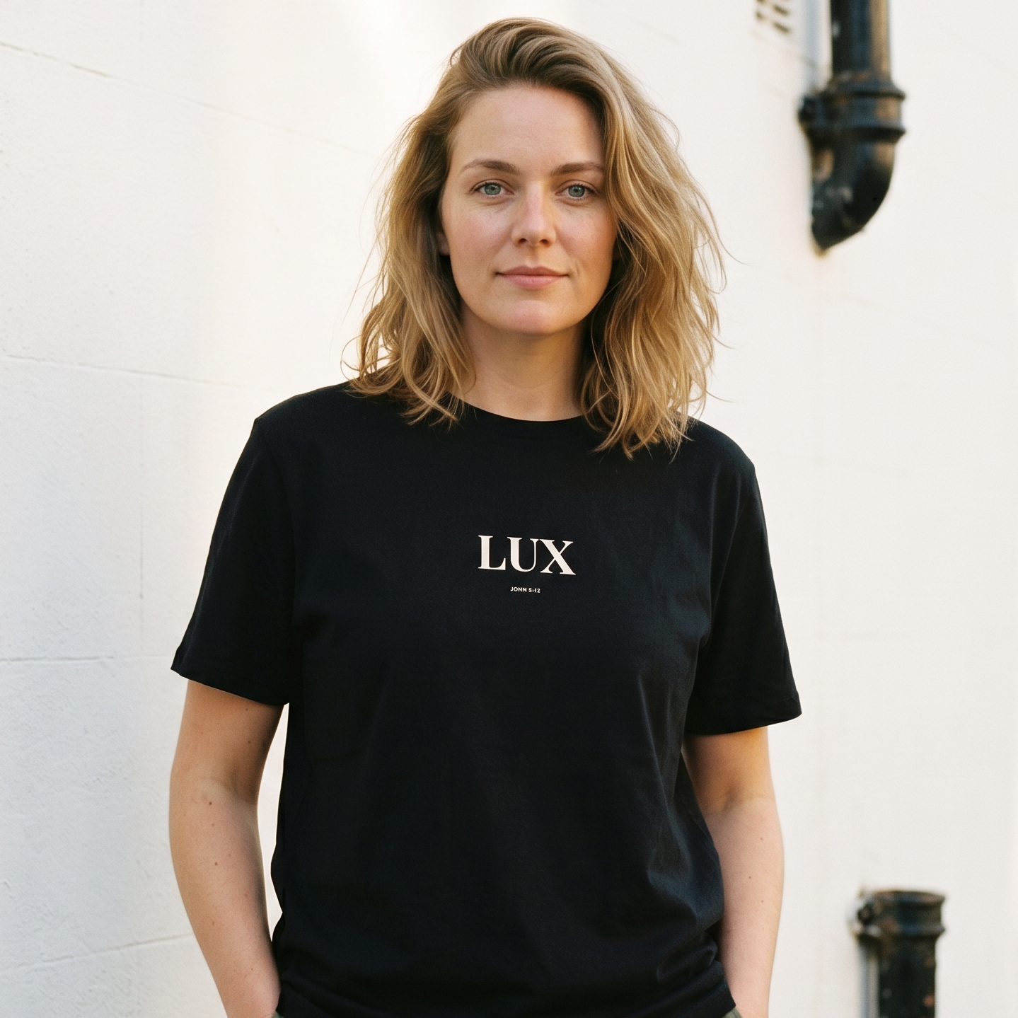 Woman wearing a black t-shirt with 'LUX' logo against a white wall.