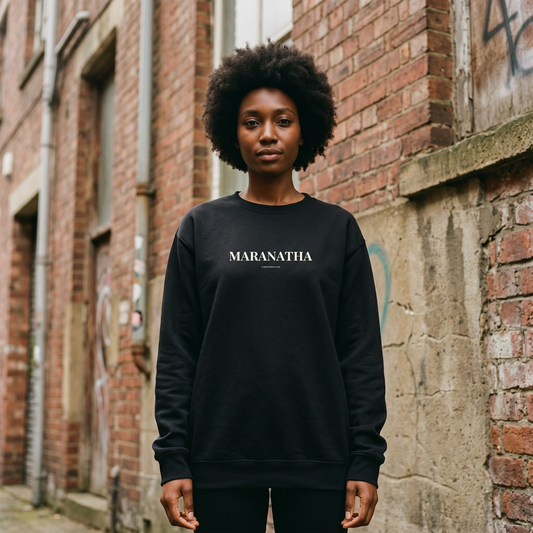 Person wearing a black sweatshirt with 'MARANATHA' text, standing against a brick wall.