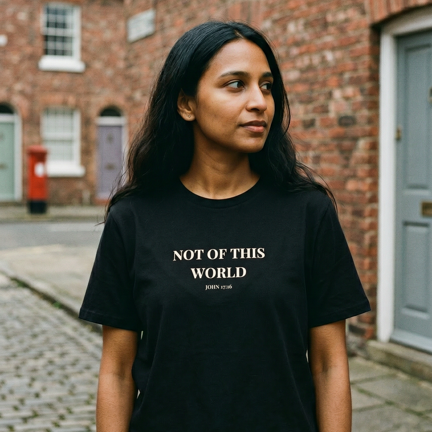 Person wearing a black t-shirt with 'Not of This World' text on a street.