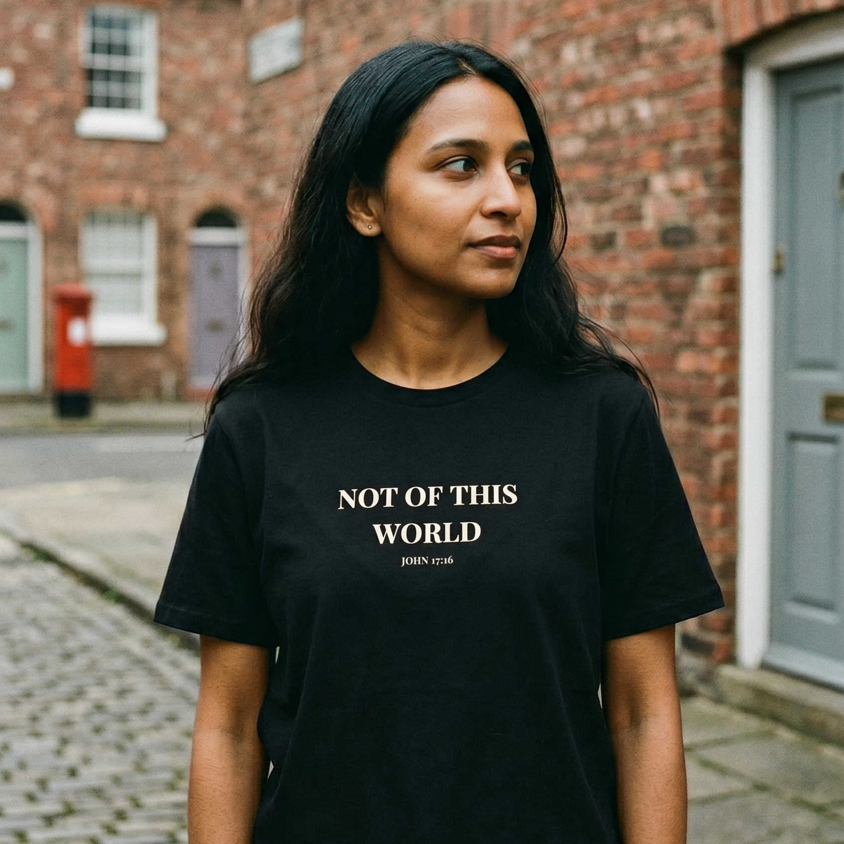 Person wearing a black t-shirt with 'Not of This World' text on a street.