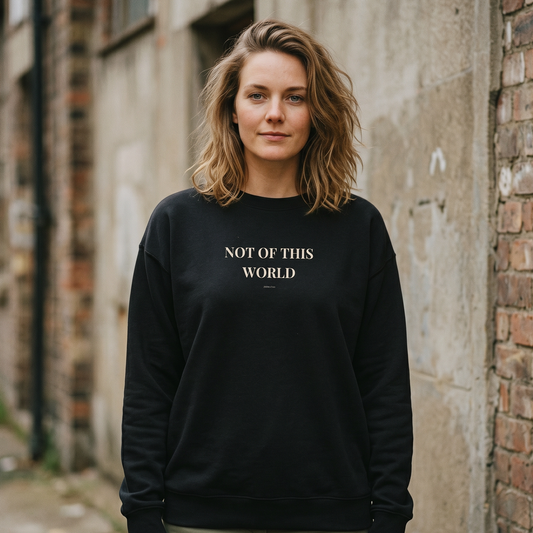 Woman wearing a black sweatshirt with 'NOT OF THIS WORLD' text, standing against a brick wall.