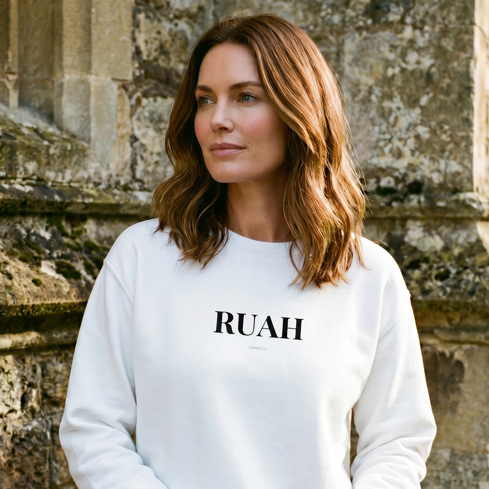 Woman wearing a white sweatshirt with 'RUAH' text, standing in front of stone architecture.
