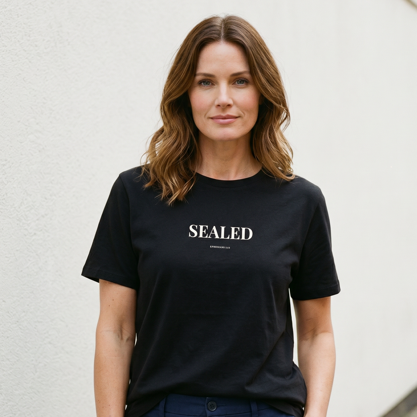 Woman wearing a black t-shirt with 'SEALED' text against a light-colored wall.