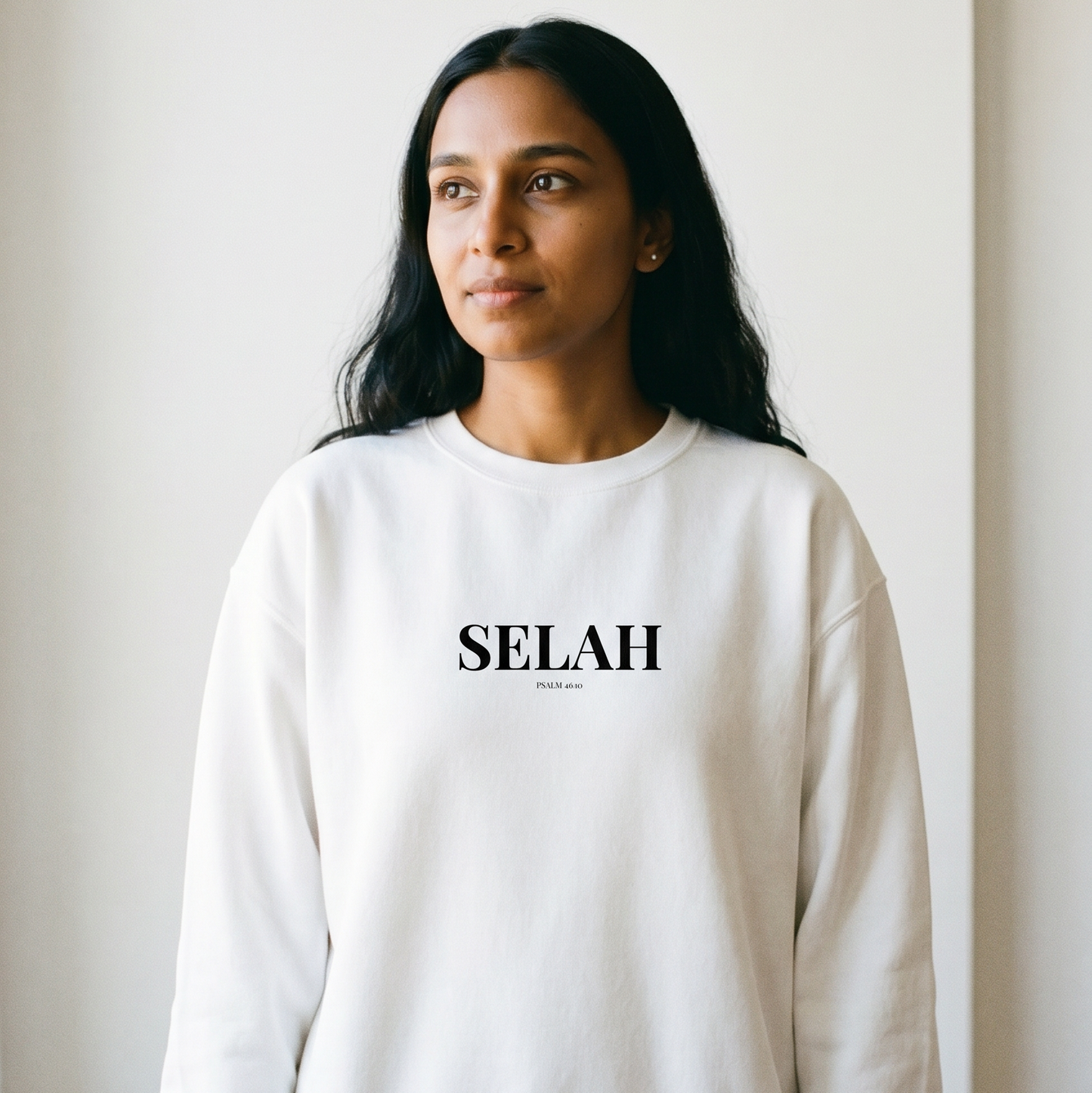 Woman wearing a white sweatshirt with 'SELAH' printed on it against a plain background