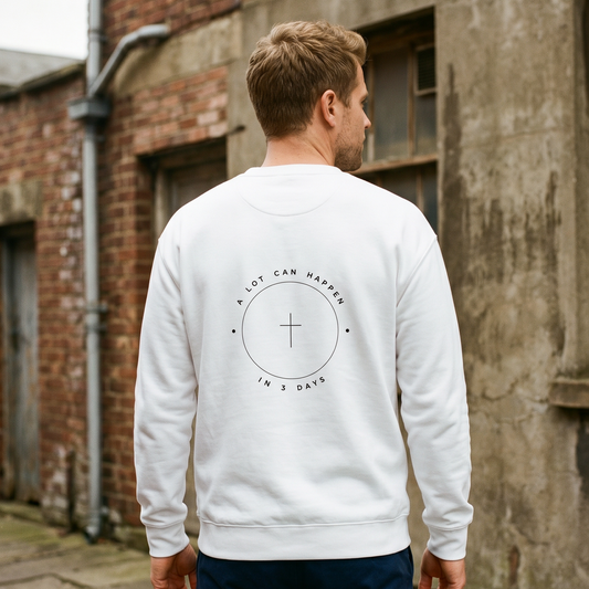 Man wearing a white sweatshirt with a design on the back, standing in front of a brick wall.