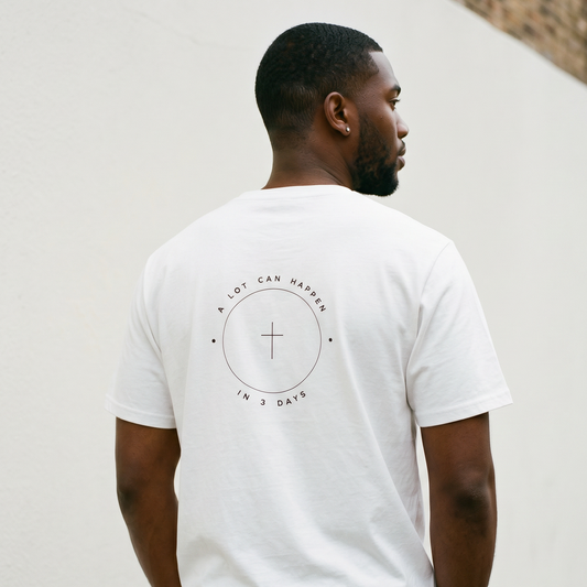 Man wearing a white t-shirt with a circular design and text on the back, standing against a light-colored wall.