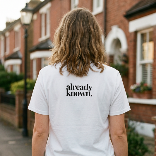 Person wearing a white t-shirt with 'already known' text on the back, standing on a residential street.