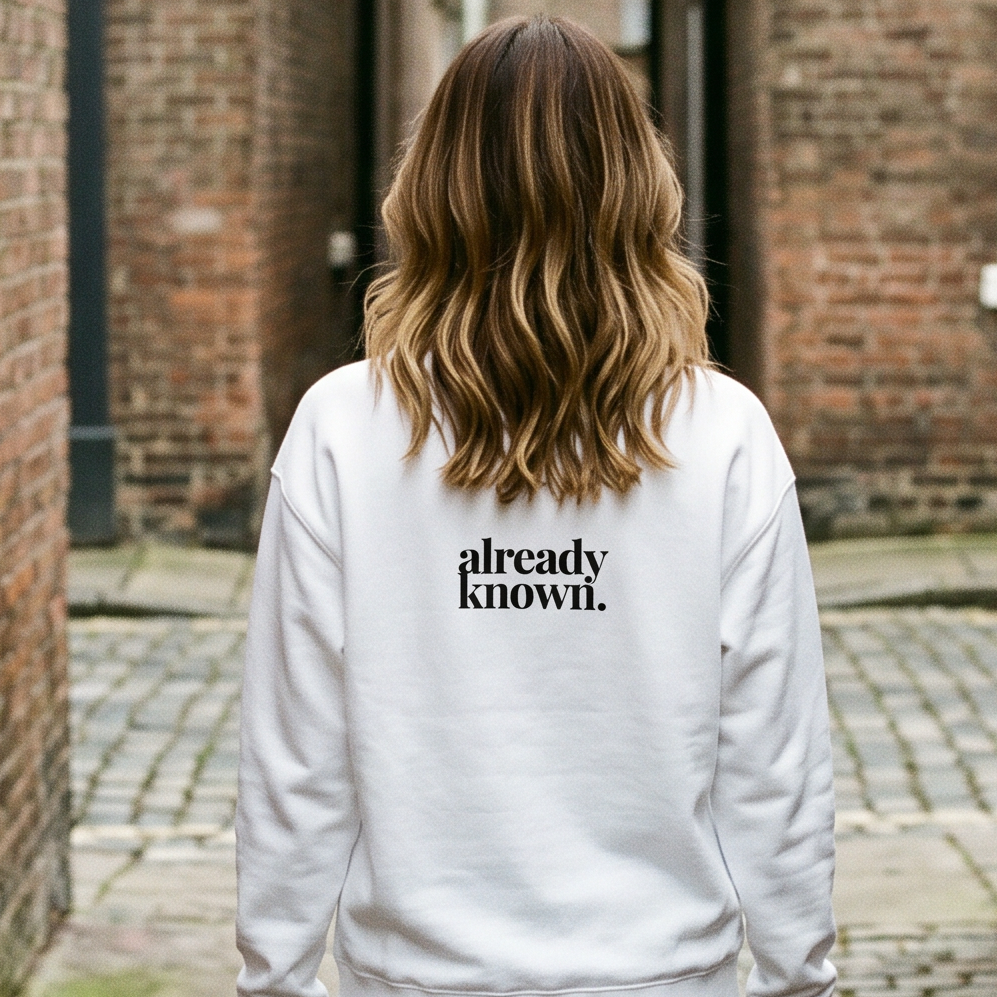 Person wearing a white sweatshirt with 'already known' text walking down a narrow brick alley.