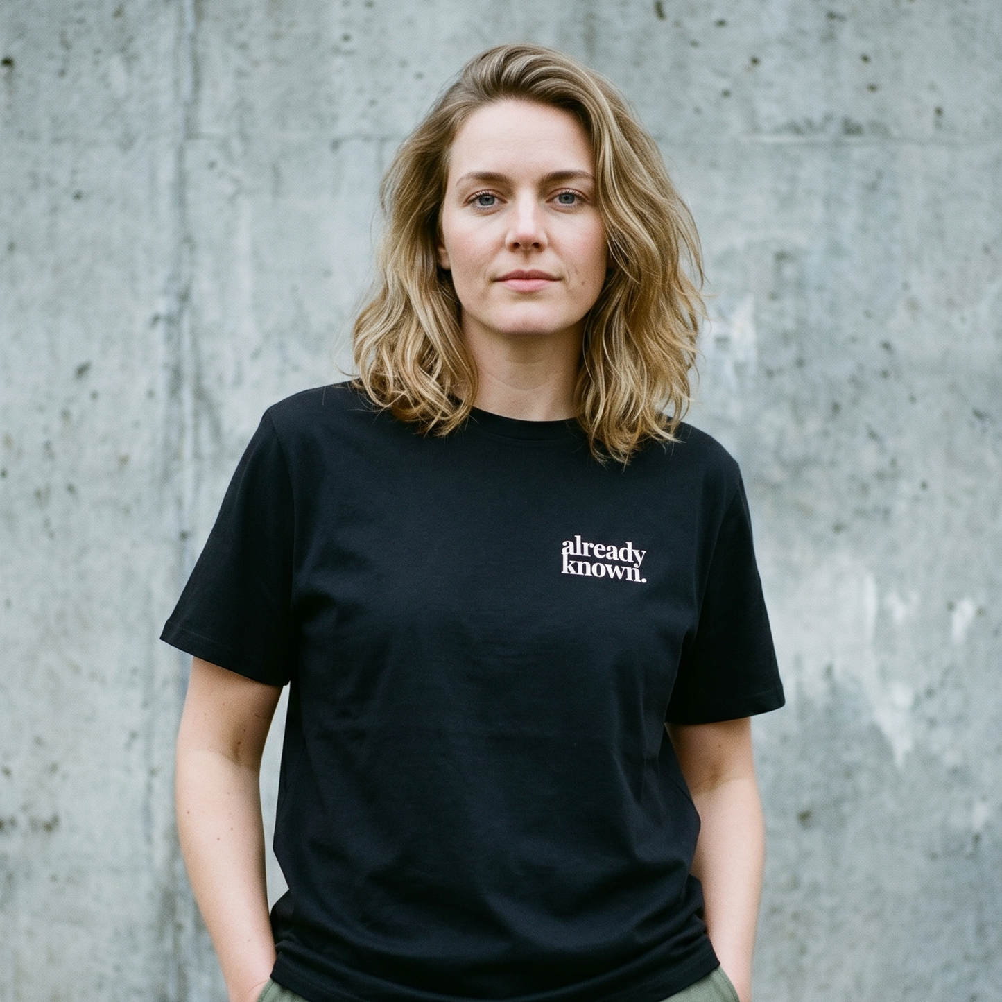 Person wearing a black t-shirt with 'already known' text against a concrete wall.