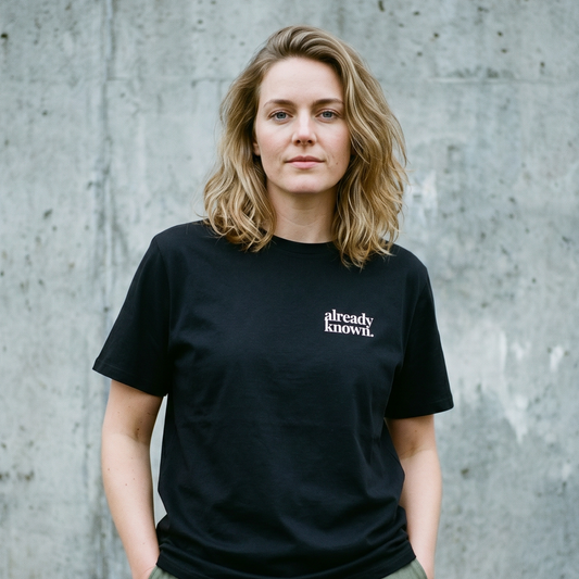 Person wearing a black t-shirt with 'already known' text against a concrete wall.