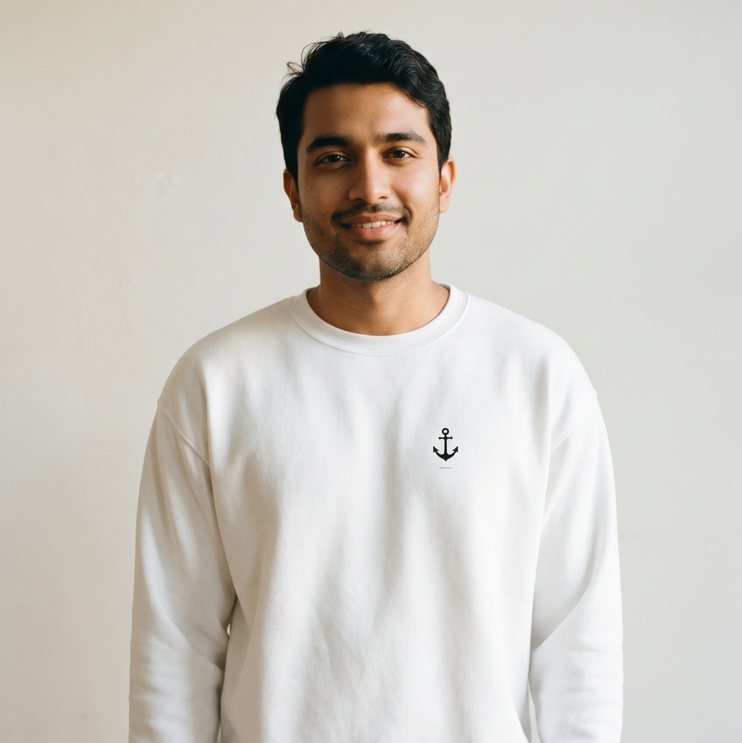 Man wearing a white sweatshirt with an anchor emblem against a plain background