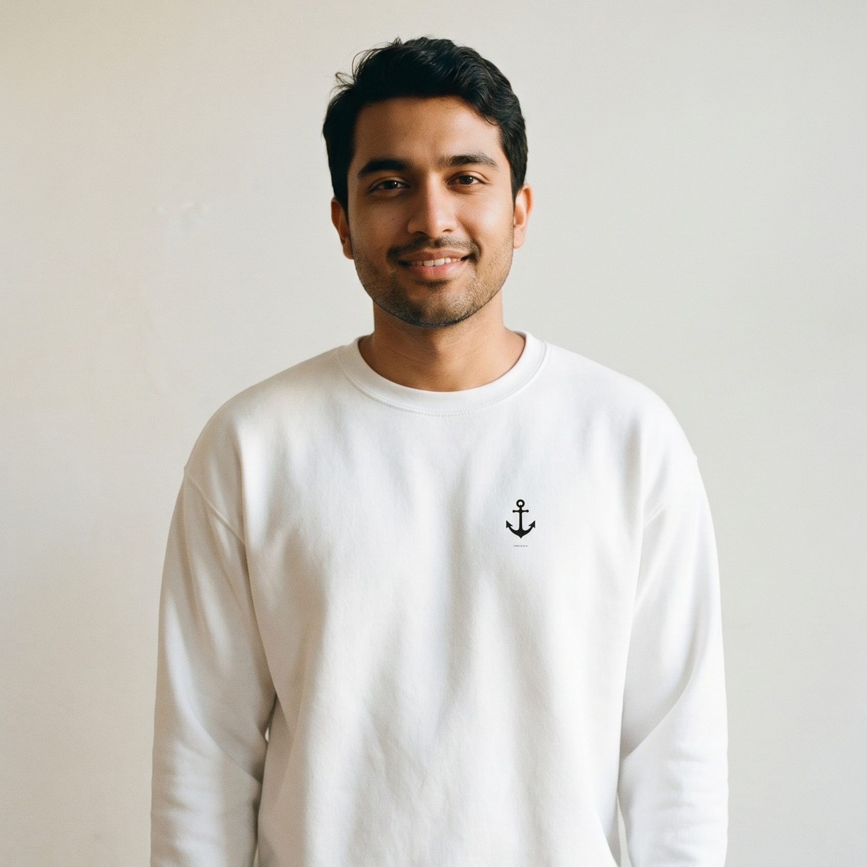 Man wearing a white sweatshirt with an anchor emblem against a plain background