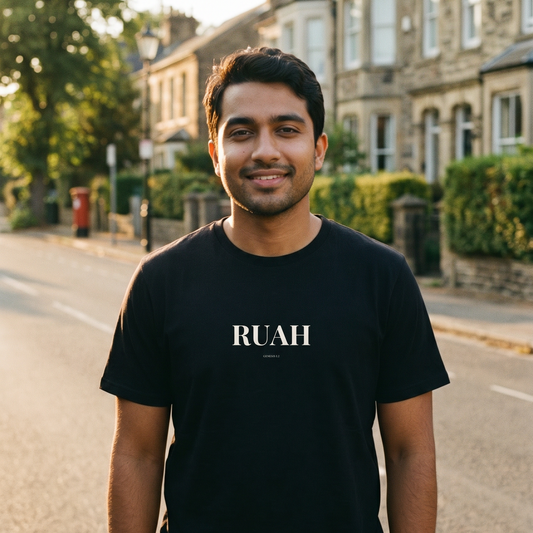 Man wearing a black t-shirt with 'RUAH' printed on it, standing on a street.