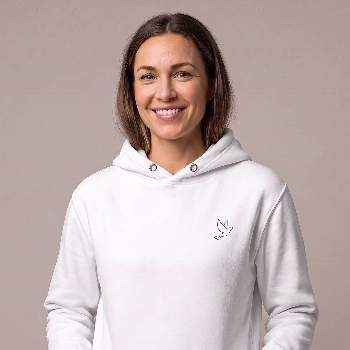 A woman wearing a white pullover hoodie with a small black line-art dove logo on the left chest, standing against a solid beige background.