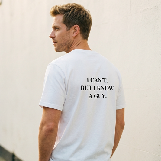 Man wearing a white t-shirt with text on the back, standing against a light-colored wall.