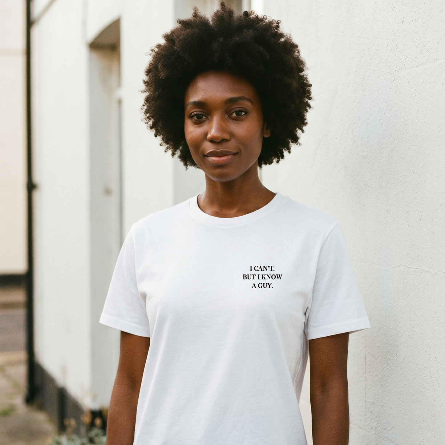 Person wearing a white t-shirt with text, standing against a light-colored wall.