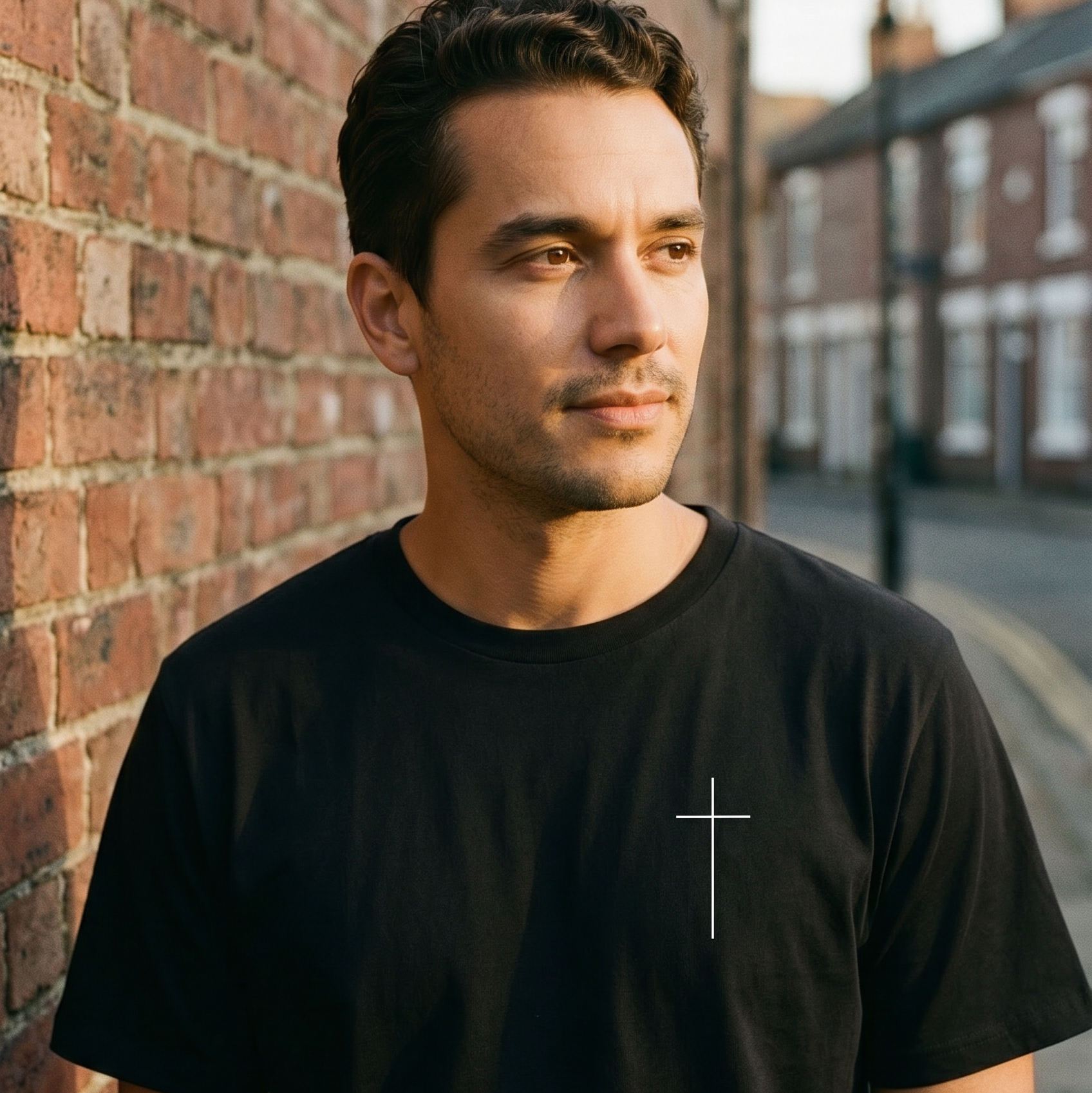 Man wearing a black t-shirt with a cross design against a brick wall.