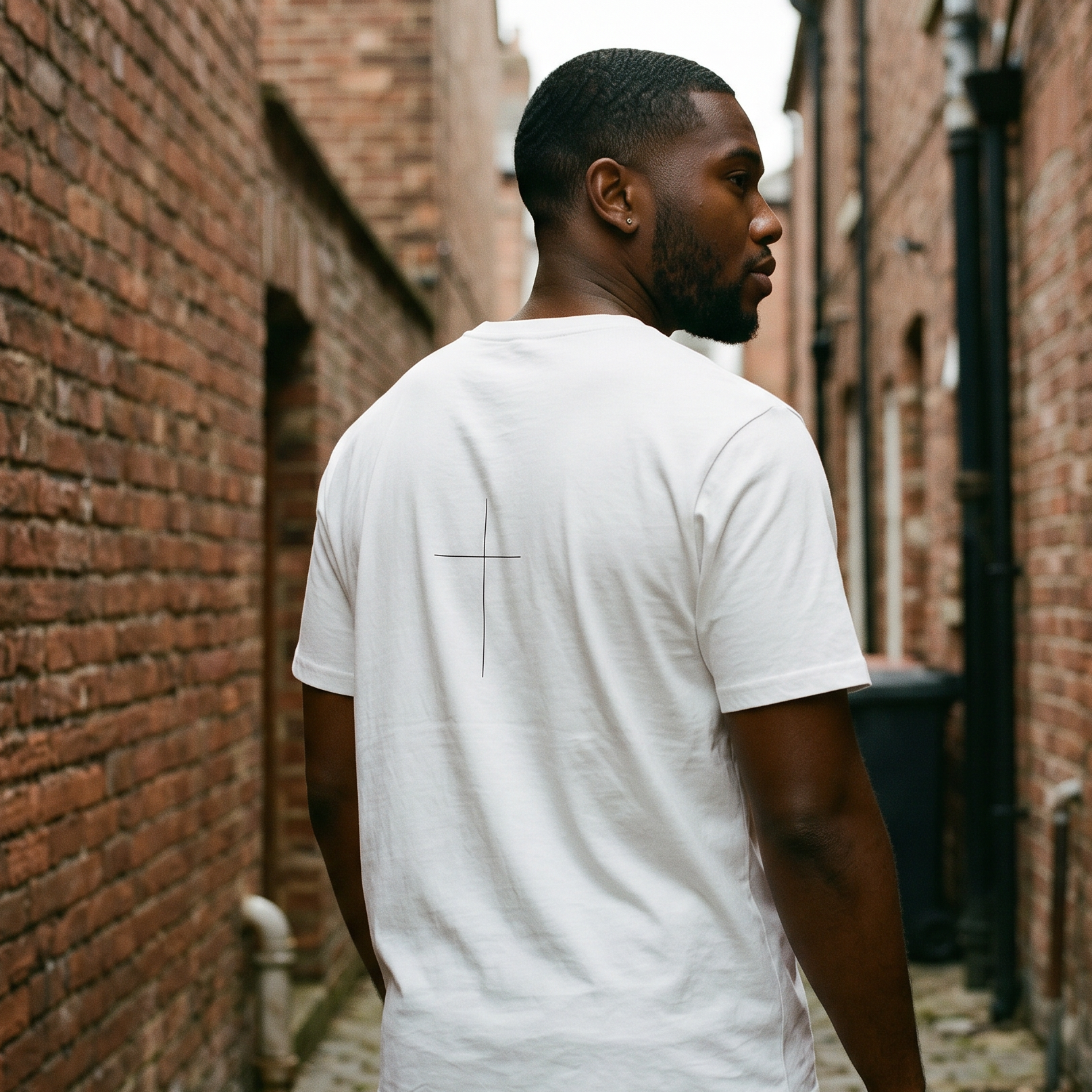 Man wearing a white t-shirt walking down a narrow alley between brick walls.