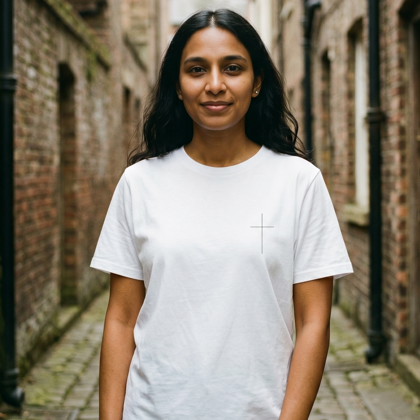 Woman wearing a white t-shirt standing in a narrow alley with brick walls.